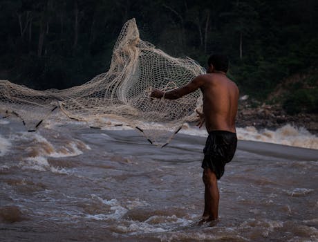 A man skillfully casts a fishing net into the rushing waters of a river in Tarapoto, Peru.