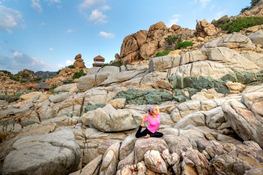 A woman is practicing yoga on rocky terrain under a clear sky, highlighting a serene outdoor setting.