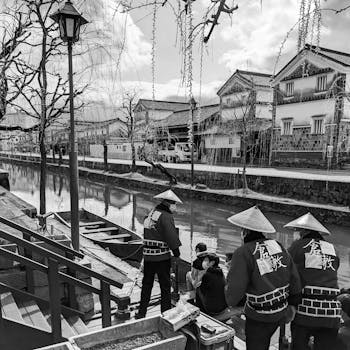 Black and white image of people by a canal with Japanese architecture.