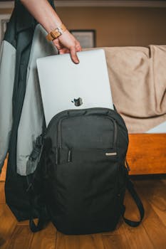 Close-up of a person placing a laptop into a black backpack indoors.