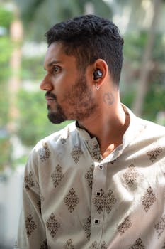 Portrait of a young man wearing wireless earbuds, outdoors, in a casual outfit.