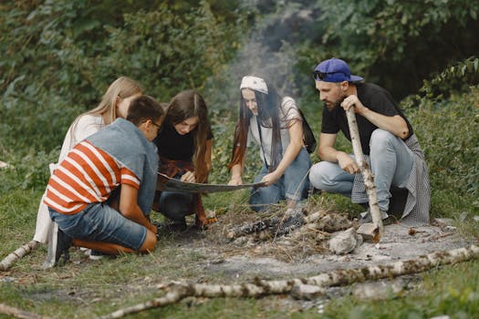 A diverse group of young adults gather around a campfire, exploring a map during a hiking adventure.