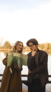 A stylish couple in coats holding a map by the lakeshore, planning their next adventure.