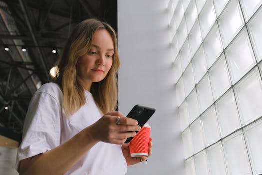 Blonde woman holding a coffee cup and phone indoors with stylish design.