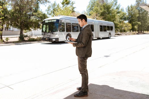 Businessman in corporate attire using laptop outdoors near bus stop, signifying remote work flexibility.