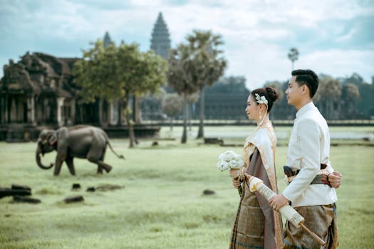 Elegant Cambodian couple in traditional attire at Angkor Wat with an elephant in the background.