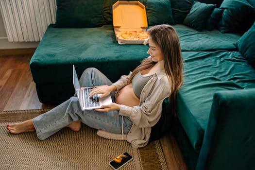 Expectant mother working from home on a laptop, sitting comfortably on the floor near a couch.