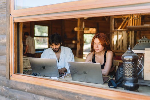 Two professionals working on laptops in a cozy cottage with natural light streaming in.